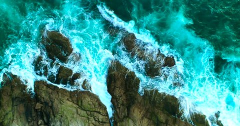 Aerial: Beautiful sea waves with white foam on rocky coastline are crashing against big stones. Thailand.