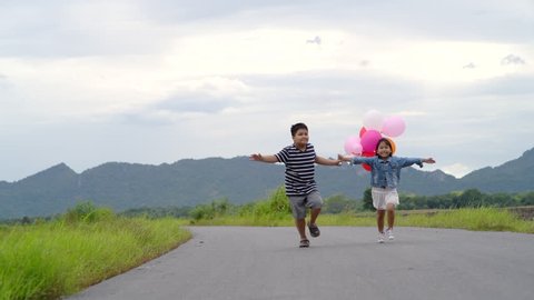 Brother and sister with balloons running on the road, lifestyle concept