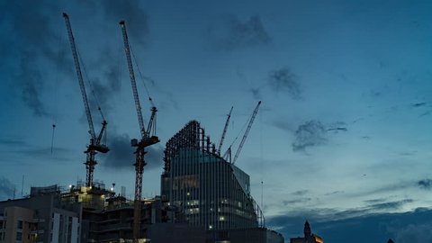 Timelapse Construction the buildings. Construction Process of Skyscraper  with cranes on the roof and clouds on a blue sky. Day to Night Time lapse 4K.