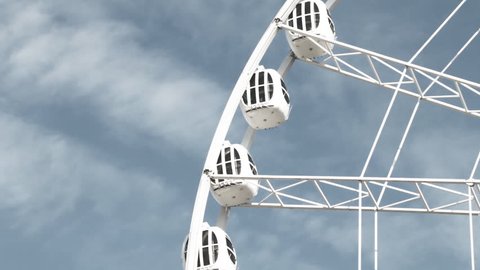 Rotating Ferris wheel against the blue sky and clouds: piece of whole structure with cabins/capsules. Concept of growth, freedom, height. Black and white.