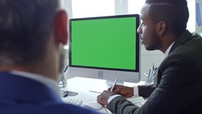 African American businessman sitting at meeting table in the office, speaking with colleagues and video calling on computer with chroma key screen
