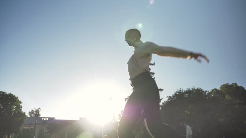 Silhouette of young extraordinary bold girl is dancing on grass in park in daylight in summer, movement concept, bottom view