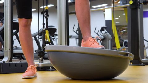 A fit woman tries a bosu ball with her leg in a gym - closeup