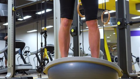 A fit woman does squats on a bosu ball in a gym - closeup on the legs