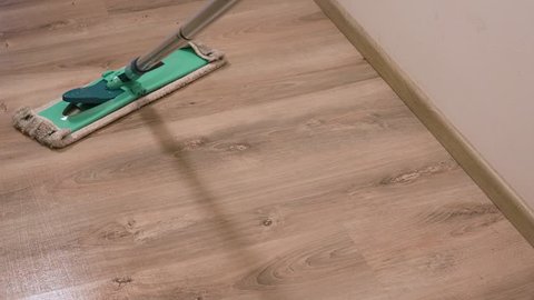 A woman mops a floor in an apartment hall - closeup on the mop from above