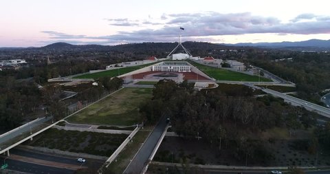 Capitol hill in government district of Canberra at sunset in aerial panning in front of new parliament house under national flag.
