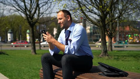 Businessman texting, sending sms on smartphone in the city park
