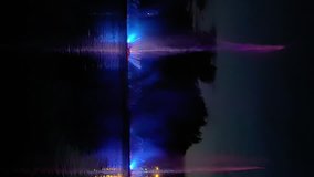 Amazing fantastic colorful fountain with bright illumination on the water pond or river with beautiful reflection at the evening or night. Beauty urban recreational concept. Vertical format video.
