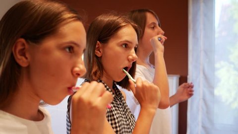 Brush teeth in front of the bathroom mirror three girls teenager sisters before going to bed