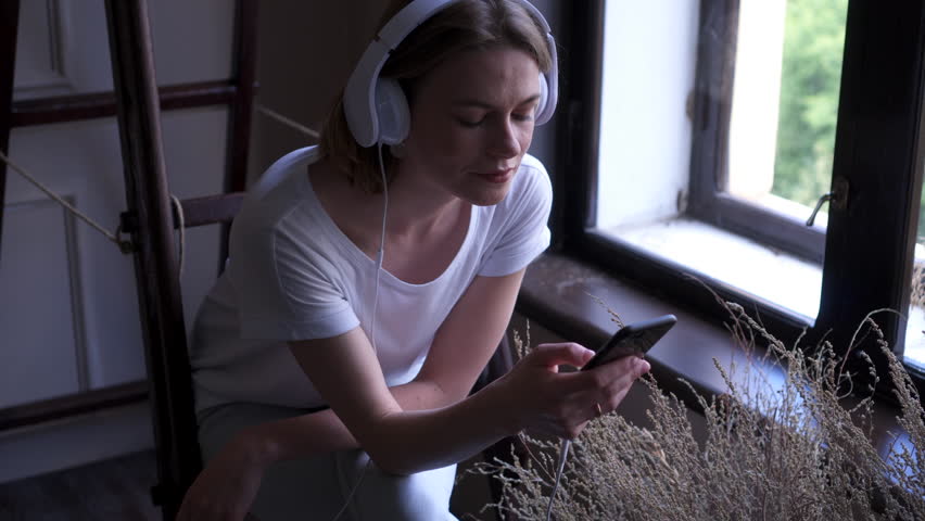 Young attractive girl enjoying music sitting near window