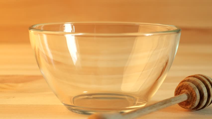 Honey pouring into glass bowl on wooden background, close up 4K