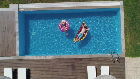 Aerial - Couple relaxing on inflatable donut and watermelon floatie in the pool at home