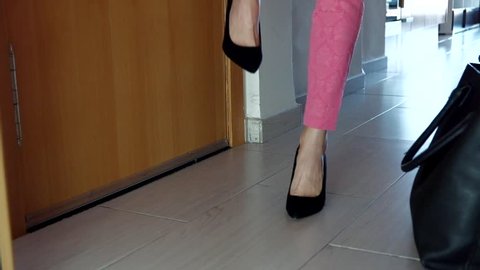 Close-up of young woman taking off unsuitable high heels shoes and relaxing her feet after coming home from work. Slow motion.
