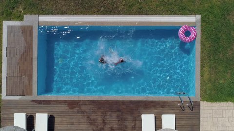 Aerial - Couple holding hands and jumping in the pool like a cannon ball