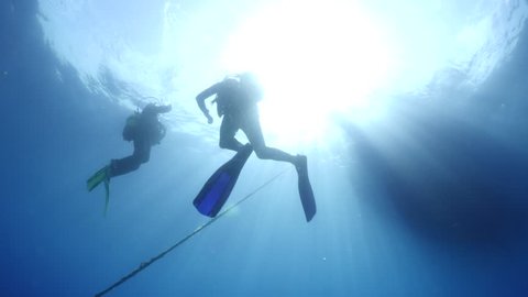scuba divers ascending to the surface to the dive boat with sun beams and rays underwater 
