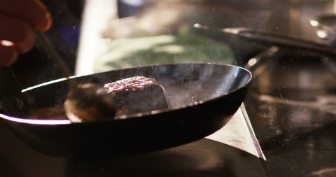 Slow motion of middle aged chef mixing salsa of fried meat fillet with wooden spoon in a pan in a restaurant kitchen (close up)