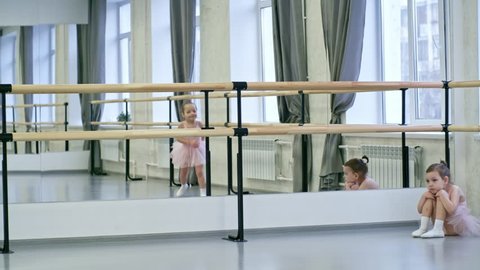 Little girl sitting sad and tired on the floor and looking at other girls who are jumping around in dance class