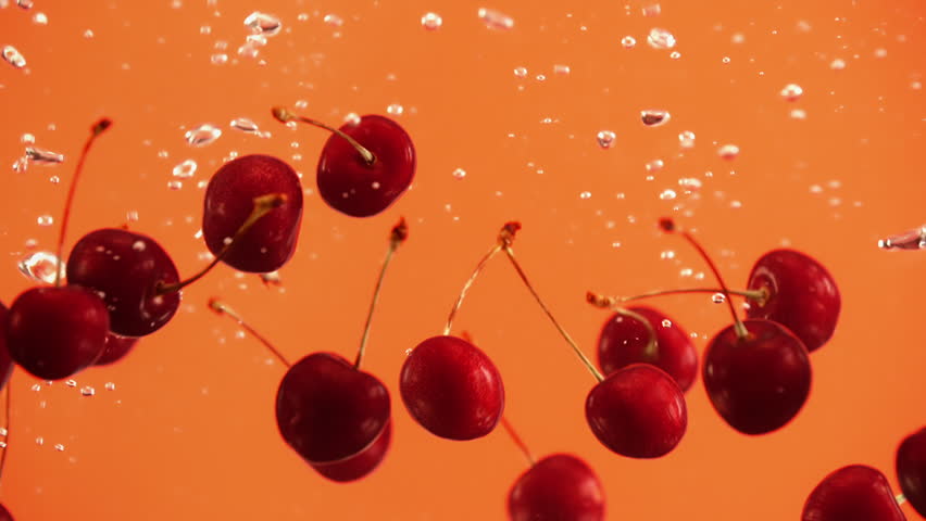 Close up of ripe cherries cherry fall into water on orange background. Red berries in liquid | Shutterstock HD Video #1012343324