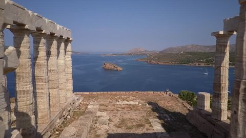 Beautiful Greek temple Poseidon at Cape Sounion Greece. Drone aerial view through inside the old building. Bay with sailing boats in background. Sunny day and Islands
