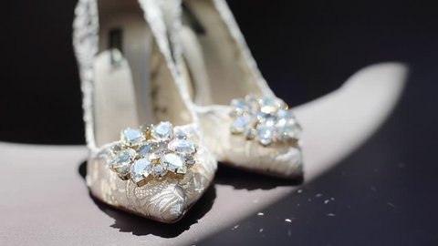 White lace designer shoes for woman standing indoors shining precious diamonds stones slow motion. Female wedding footwear waiting princess black background close up copy space. Bridal fashion

