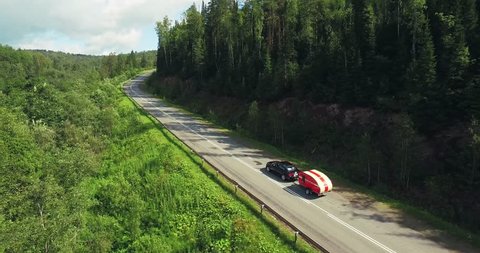 One Black Car with Funny Tear Trailer driving on Winding Freeway in Forest Mountains - Aerial Drone View Arkivvideo