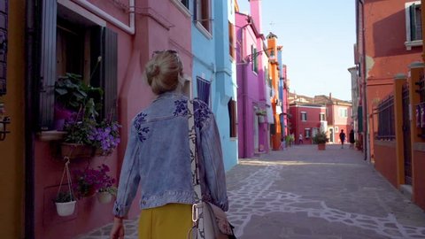 Young woman walking in colorful streets of Burano, Italy during sunset	
