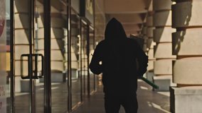Mysterious hooded man running wirh poster in hand in city . Camera gimbal motion . View from the back . Shot on ARRI ALEXA Cinema camera in Slow Motion.