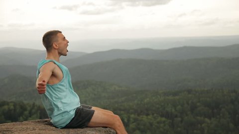 A man sits on the edge of a cliff and shouts.