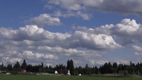 Landscape of a green field with village houses and moving white clouds on a blue sky. Time lapse video full hd.