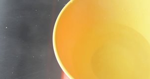 Close video of pouring orange flavor gelatin mix into a yellow bowl with hot water on a stainless steel counter top.