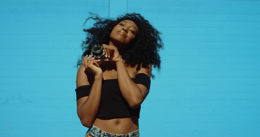Beautiful young woman shooting photos with film camera against colorful blue wall