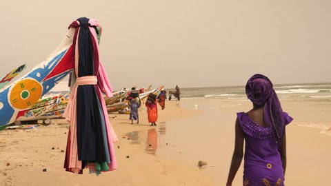 Africa: fishermen's beach with colorful fishing boats and women in traditional dress in Senegal.