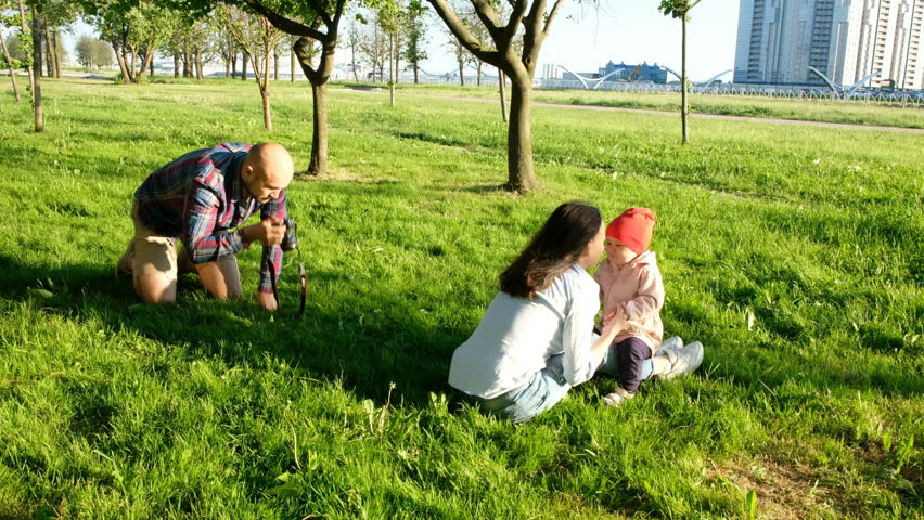 Young father photographing kissing mother and daughter in the park at sunset. Happy family taking photos in nature