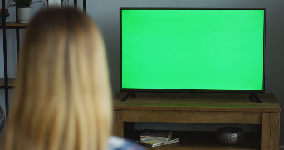 View from the back on the blonde woman sitting in the living room and watching TV with green screen. Chroma key. Indoor | Shutterstock HD Video #1012385417
