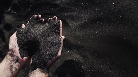 Woman pours sand from her hand on black beach. Sand shining like diamonds