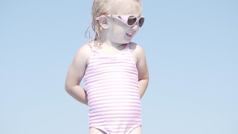 a little girl stands on the edge of the pool and prepares to jump into the water. On the girl a swimsuit white in pink stripes and pink glasses with dolphins