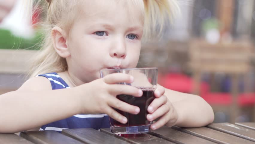 Little girl is drinking juice in a cafe. A girl sits at a table and drinks cherry juice from a straw Royalty-Free Stock Footage #1012390610