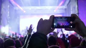 fans with mobile phones into hands delight live music at rock concert in bright scene lights in evening