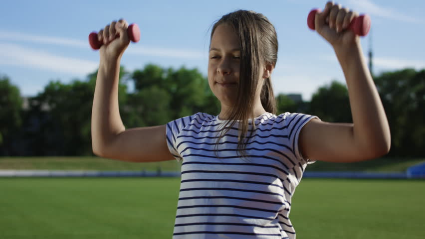 From below view of teen girl and boy doing exercises with light dumbbells standing in sunlight outside