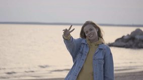 Caucasian young girl with beautiful smile making video on the beach using the drone flying above the sea. Sunset scene, autumn windy weather. Travel concept of freedom and happiness slow motion