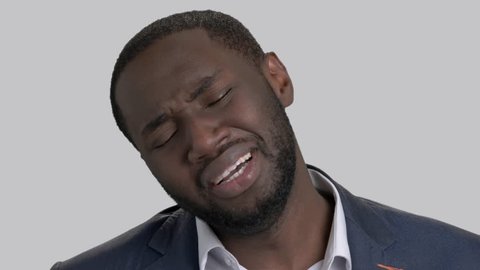 Crying black businessman in full despair. Face of unhappy desperate afro-american businessman is wiping tears on grey background close up. Stress and sorrow.