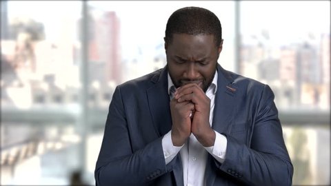 Afro-american businessman is crying on blurred background. Stressed dark-skinned man in business suit is crying. Black entrepreneur is praying.