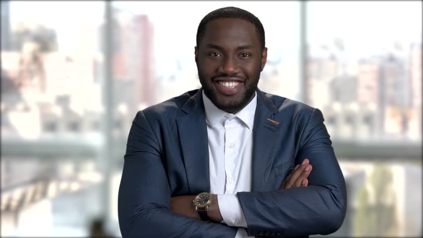 Stylish afro-american businessman with arms crossed. Smiling dark-skinned entrepreneur posing on blurred background.