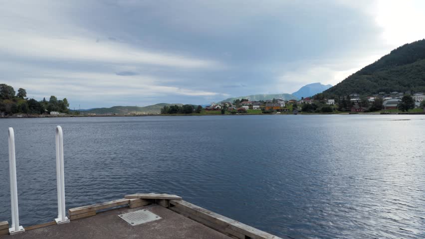 Man looking at beautiful scenery or seascape. Fishing town, village, settlement in Norwegian fjord. Calm water surface, high mountains covered with dense green forest, clear blue sky