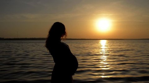 Pregnant woman standing at sunset on the river