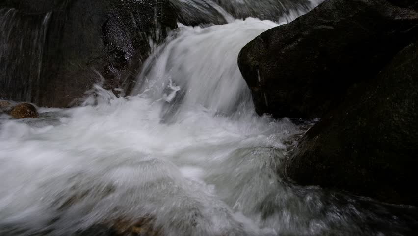 Closeup. The stream flows water with brown rocks. 