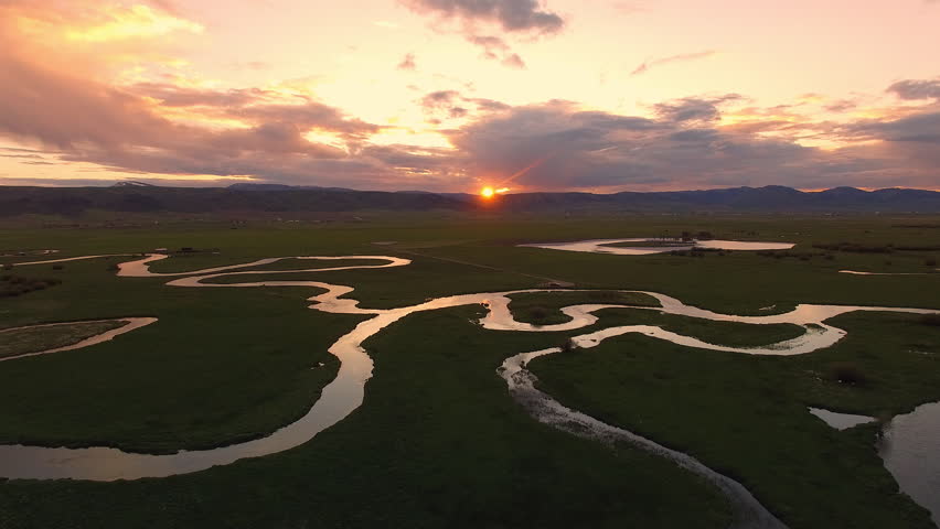 Aerial view flying over winding river during colorful sunset in Star Valley Wyoming.
