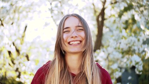 Beautiful happy Ukrainian girl holding flowering twigs in hands, hiding face. Young attractive Caucasian woman looking at camera, laughing in the garden. Village. Springtime. Close-up. Vídeo Stock