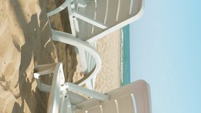 White chairs are placed on the beach for people to relax or sunbath. Beaches make a wonderful vacation spot. One of the most beautiful sceneries. Vertical format video.