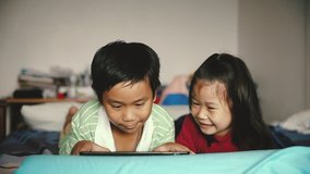 Asian children using digital tablet. Happily sister hugging and cheering her brother. Cute boy playing games excitedly on touchpad. Cinematic tone.